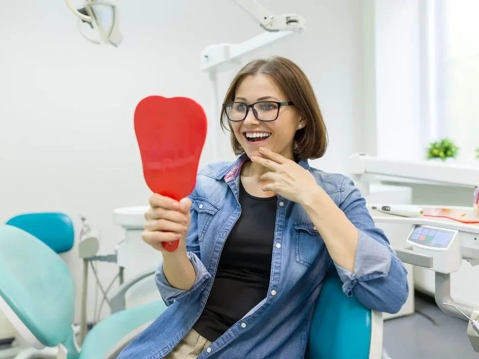 Young woman smiling in mirror after a teeth cleaning at Jamestowne South Dental